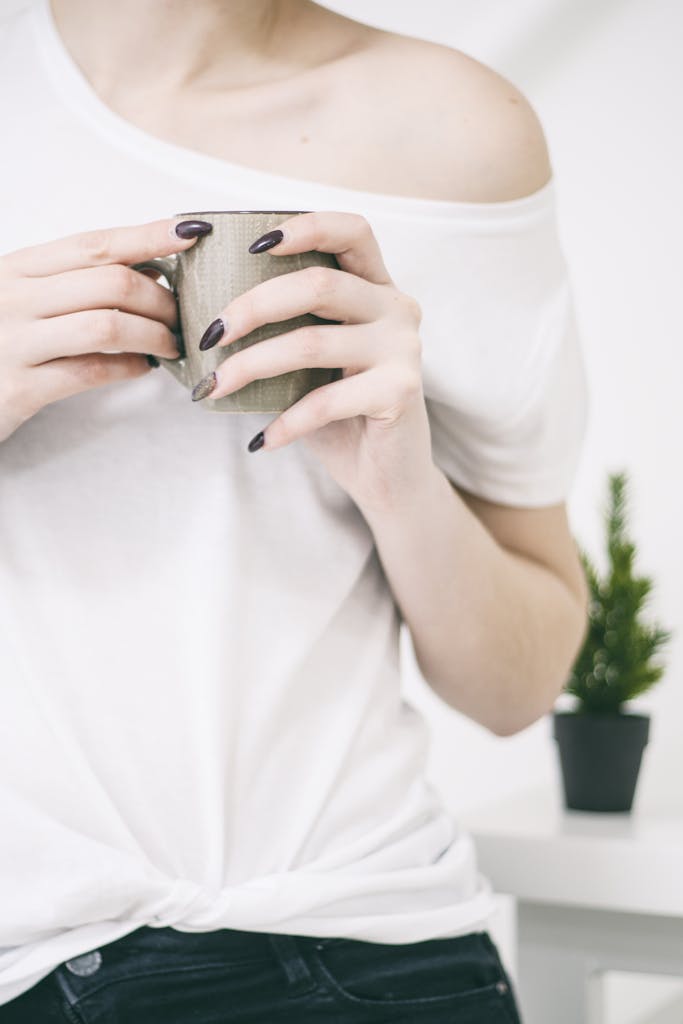 Close-up of a woman with manicured nails holding a mug in a bright, minimalist setting.