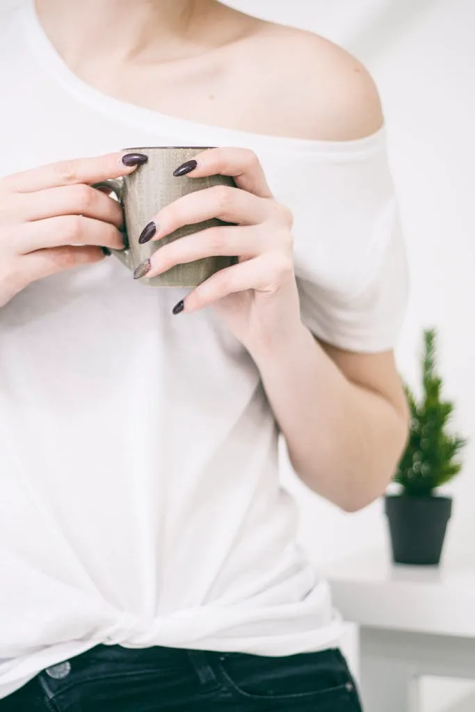 Close-up of a woman with manicured nails holding a mug in a bright, minimalist setting.
